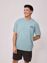 Remera holgada de algodón color beige, de manga corta y cuello redondo, con un gran estampado colorido en la espalda con diseño de olas y la inscripción 'Rusty Tribe'.