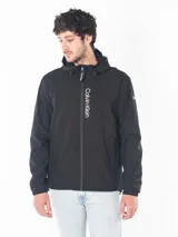 Campera rompeviento Calvin Klein de color negro, con cierre frontal, capucha ajustable y logo estampado verticalmente en el frente. Presenta puños elásticos y un parche con el logo en la manga.