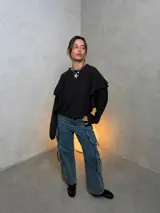 Sweater negro de textura acanalada con diseño de volados en los hombros y mangas largas. Presenta un corte holgado y cuello redondo.