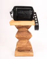 Bandolera negra de charol con doble compartimento, bolsillo frontal, correa regulable con ojalillos y detalles metálicos plateados.