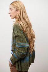 Sacon de tejido de punto grueso con diseño de ochos y rayas horizontales en contraste. Presenta cuello en V, cierre frontal con botones oscuros y mangas largas con puños acanalados.