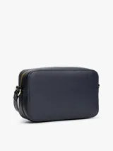 Cartera tipo bandolera de Tommy Hilfiger, confeccionada en poliuretano color azul marino. Presenta un diseño rectangular con una franja vertical central en colores blanco, azul y rojo, y el logo monograma TH en metal dorado en el frente. Incluye correa ajustable y cierre superior.