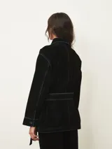 Chaqueta de terciopelo en color azul oscuro, con corte recto, cuello camisero, cierre frontal con botones metálicos y costuras a la vista en contraste. Presenta bolsillos frontales tipo parche.