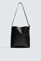 Bolso tipo shopper de cuero sintético negro, con costuras visibles en el frente que dividen el cuerpo en paneles. Presenta un borde superior ondulado y un asa de hombro ajustable.