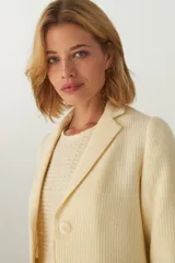 Chaqueta marrón de lana con cuello, solapa y bolsillos ojal. Forro solo en las mangas y terminaciones envivadas. Esquinas redondeadas y mangas con corte en puño que permiten transformarla en manga 3/4. Más larga en la espalda que en la delantera. Abrochadura con dos botones.