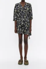 Vestido corto negro con estampado paisley en tonos amarillo y lila, escote en pico pronunciado con fruncido, manga larga con botón en puño, cierre con cremallera invisible, cintura con maxifruncido y falda con vuelo.