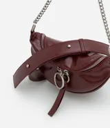 Cartera tipo riñonera de tamaño pequeño, confeccionada en poliuretano con acabado brillante. Presenta un diseño de media luna con cierre de cremallera metálica, decorado con tiradores circulares. Incluye una correa de cadena metálica para llevar al hombro o cruzada.