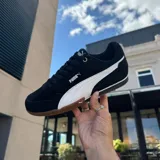 Championes Puma modelo Bella Donna, de diseño urbano y deportivo en color negro con la icónica franja lateral en blanco. Presenta una suela de goma color caramelo con excelente tracción y detalles en dorado en los ojales de los cordones.