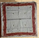 Pañuelo de seda estampado con diseño ecuestre que combina un centro gris con rombos oscuros, bordes en bordó y detalles de cinturones y cabezas de caballo.