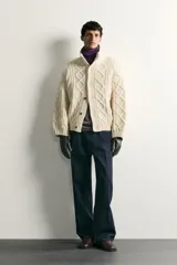 Jersey relaxed fit de punto tejido en hilatura de lana color blanco, con cuello subido, manga larga y acabados en rib. Presenta diseño de trenzas y cierre frontal con botonadura oculta.