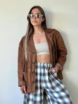 Chaqueta de estilo boho confeccionada en ecocuero agamuzado, con diseño de flecos en el frente, cierre frontal con botones y bolsillos laterales. Presenta un corte holgado y forro interior.