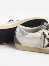 Zapatillas Golden Goose modelo Super-Star, con pala de cuero blanco, estrella con purpurina color burdeos, refuerzo del talón de piel laminada plateada, aplicaciones de ante gris paloma y cordones con estampado de leopardo en tonos beige y marrón.