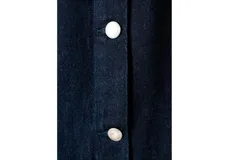 Mono largo de denim color azul oscuro, con cuello redondo, manga larga y cierre frontal de botones metálicos. Presenta corte recto y holgado en las piernas.