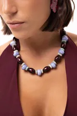 Collar corto compuesto por cuentas alternadas de color bordó brillante, celeste pastel y gris claro. El diseño presenta una combinación de materiales que incluyen acrílico, cerámica y piedras naturales.