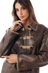 Campera estilo militar napoleón confeccionada en cuero ovino, con cierre frontal y solapa decorativa con botones metálicos y alamares de gamuza en tono crudo. Cuenta con cuello camisero, pespuntes visibles y diseño estructurado de manga larga.