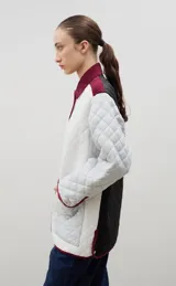 Campera acolchada de corte holgado, color blanco con diseño capitoneado en forma de rombos. Presenta cuello camisero y bordes internos con estampado floral en tonos azul y rojo, cierre frontal con botones a presión y bolsillos laterales.