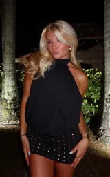 Vestido corto negro con cuello halter y diseño drapeado en la parte superior. La falda presenta un ajuste ceñido con detalle de tachas metálicas doradas distribuidas por toda la superficie.