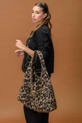 Bolso tipo hobo de gran capacidad, confeccionado en tela suave con estampado animal print de leopardo. Cuenta con un diseño de caída relajada y una etiqueta distintiva en el frente.