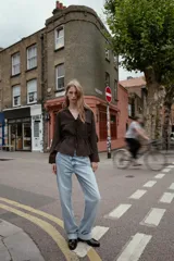 Botín de cuero sintético negro con caña elástica lateral, tirador trasero y detalle de aplique metálico dorado en la base del tacón cuadrado.