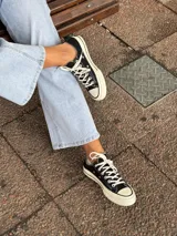 Zapatillas bajas de lona color negro con cordones blancos y suela de goma color crema.