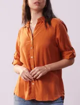 Camisa color ladrillo de tencel, marca Hester & Orchand. Cuello con solapa, escote en V y abertura central con botones. Delantera con bolsillos. Largo de manga regulable con presilla y botón.