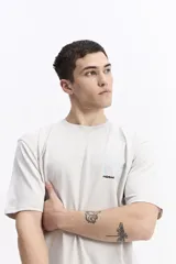 Remera de manga corta color beige claro, con cuello redondo y un estampado minimalista en el pecho que incluye la palabra "mistral" y un diseño gráfico en tonos celestes y negros.