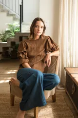 Blusa de tela texturizada color café, con cuello redondo y mangas al codo que presentan tres volados superpuestos y puños elásticos. Cuenta con cierre de botón en la parte posterior.