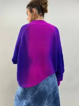 Buzo tejido de lana merino con diseño oversize, manga ranglan y cuello levemente elevado. Presenta un degradado de color vibrante en tonos violeta y fucsia.