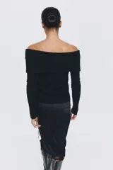Buzo de punto acanalado negro con escote off-the-shoulder y detalle de nudo frontal. Presenta mangas largas y corte ajustado.