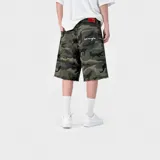 Bermuda baggy de denim con estampado camuflado en tonos verde, corte holgado, bolsillos traseros con bordado en cursiva y badana roja en la cintura.