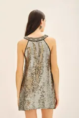 Vestido corto de corte recto y sin mangas, confeccionado en viscosa con bordado integral de lentejuelas en tonos dorados y plateados. Presenta un escote en V con una guarda bordada a mano que incluye piedras, mostacillas y lentejuelas.