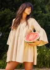 Vestido corto color beige, de lino y corte en A, con escote en V con tiras para anudar y mangas amplias.