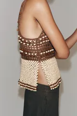 Top de crochet con escote recto y tirantes finos. Presenta un diseño bicolor con la parte superior en color marrón y la parte inferior decorada con abalorios en tonos crema y marrón.