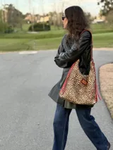 Cartera tipo hobo de cuero con estampado animal print de leopardo, con tiras y detalles en cuero rojo con flecos y parche rectangular con logo grabado en la parte frontal.