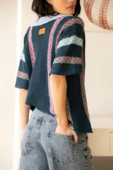 Camisa tejida de algodón a rayas verticales en tonos azul, celeste y rosa, con botones al frente y mangas cortas.