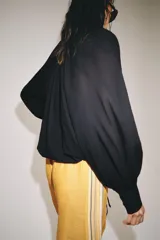 Camisa de algodón color negro, con cuello subido, manga larga terminada en puño ancho y bajo ajustable con cordones. Cuenta con cierre delantero con botones ocultos por solapa y detalles fruncidos.