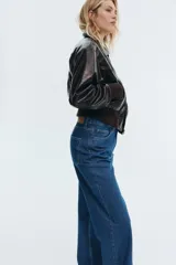 Jean de tiro alto con corte wide leg, confeccionado en denim de algodón rígido. Presenta diseño clásico de cinco bolsillos, cierre frontal con cremallera y botón, y perneras amplias con ajuste holgado desde el muslo hasta el bajo.