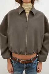 Chaqueta de corte corto y diseño abullonado en color marrón oscuro, con cuello solapa, mangas largas con puños elásticos y cierre frontal con cremallera metálica. Cuenta con bolsillos delanteros de doble vivo.