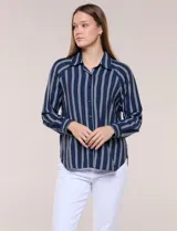 Camisa de crepe blanca con rayas verticales negras, cuello camisero, mangas largas raglán y cierre frontal con botones.