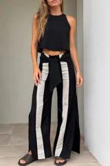 Pantalón de lino de pierna amplia, color negro con franjas verticales frontales en contraste de color beige y lazo ajustable en la cintura.