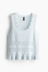 Musculosa corta celeste en tejido de punto calado estilo crochet, con escote redondo pronunciado con ribete festoneado y bajo acanalado de volado. Sin mangas.