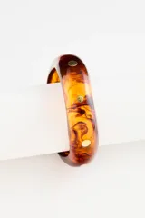 Pulsera rígida tipo brazalete de resina en tono ámbar con efecto marmolado y detalles circulares incrustados en latón dorado.