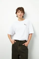 Remera negra de corte oversize con cuello redondo y manga corta. Presenta un pequeño estampado dorado en el pecho con la frase "love earth" y un símbolo de hojas.