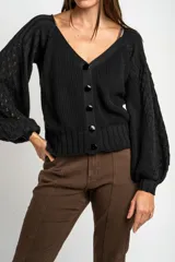Cardigan negro de algodón con cuello en V, cierre frontal de botones y mangas largas con textura calada. Presenta puños y ruedo acanalados.