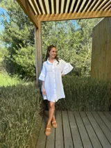 Vestido camisero blanco de lino italiano, con cuello camisero, cierre frontal con botones, mangas cortas con doble volado y bolsillos laterales.