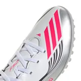 Championes de fútbol Adidas F50 Messi Club TF, diseñados para canchas sintéticas. Presentan un exterior sintético en color blanco con detalles en plateado, negro y rosa, incluyendo el logo de Messi en el lateral y las icónicas tres tiras de la marca. Su suela Turf cuenta con múltiples tapones cortos para una tracción superior.