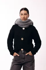 Saco de tejido de punto grueso en color negro, con cuello redondo y cierre frontal mediante tres botones metálicos grandes de acabado texturizado. Presenta bolsillos delanteros y mangas largas con puños ajustados.