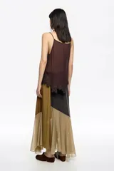 Falda larga de corte evasé con paneles asimétricos en tonos tierra, combinando telas opacas y transparentes.