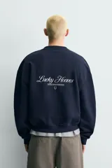 Sudadera azul marino de algodón, corte relajado (relaxed fit) con cuello redondo y manga larga. Presenta un estampado frontal en blanco con un caballo en movimiento rodeado por una cuerda y el texto "Bold Spirit".