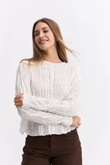 Blusa de manga larga en color blanco, confeccionada en algodón con una textura fruncida que aporta volumen y movimiento. Presenta un corte relajado y silueta suelta con caída liviana.